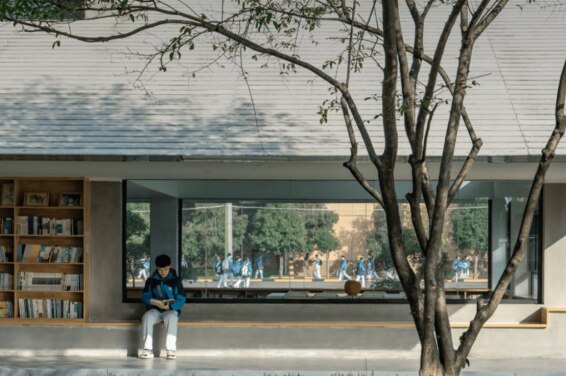一个学生坐在树荫下设有书架的空间里读书。