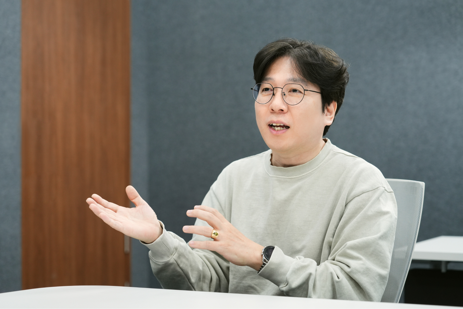 Samsung Semiconductor task leader explaining a product development concept during an interview, gesturing while seated at a conference table in a modern office setting.