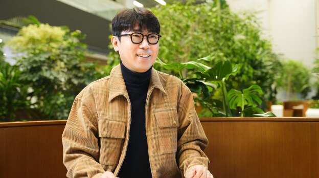 传感器设计团队的任务负责人坐在满是植物的室内工作空间里，在面试中微笑。