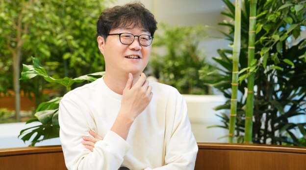 来自传感器公共广播团队的任务负责人坐在充满植物的室内工作空间里，在面试中若有所思地微笑。