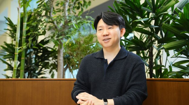 像素开发团队的一名成员坐在充满植物的室内工作空间里，在采访中微笑着说话。