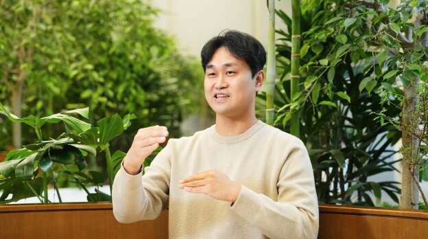 传感器解决方案团队的一名成员坐在充满植物的室内工作空间中，在面试时用手势说话。