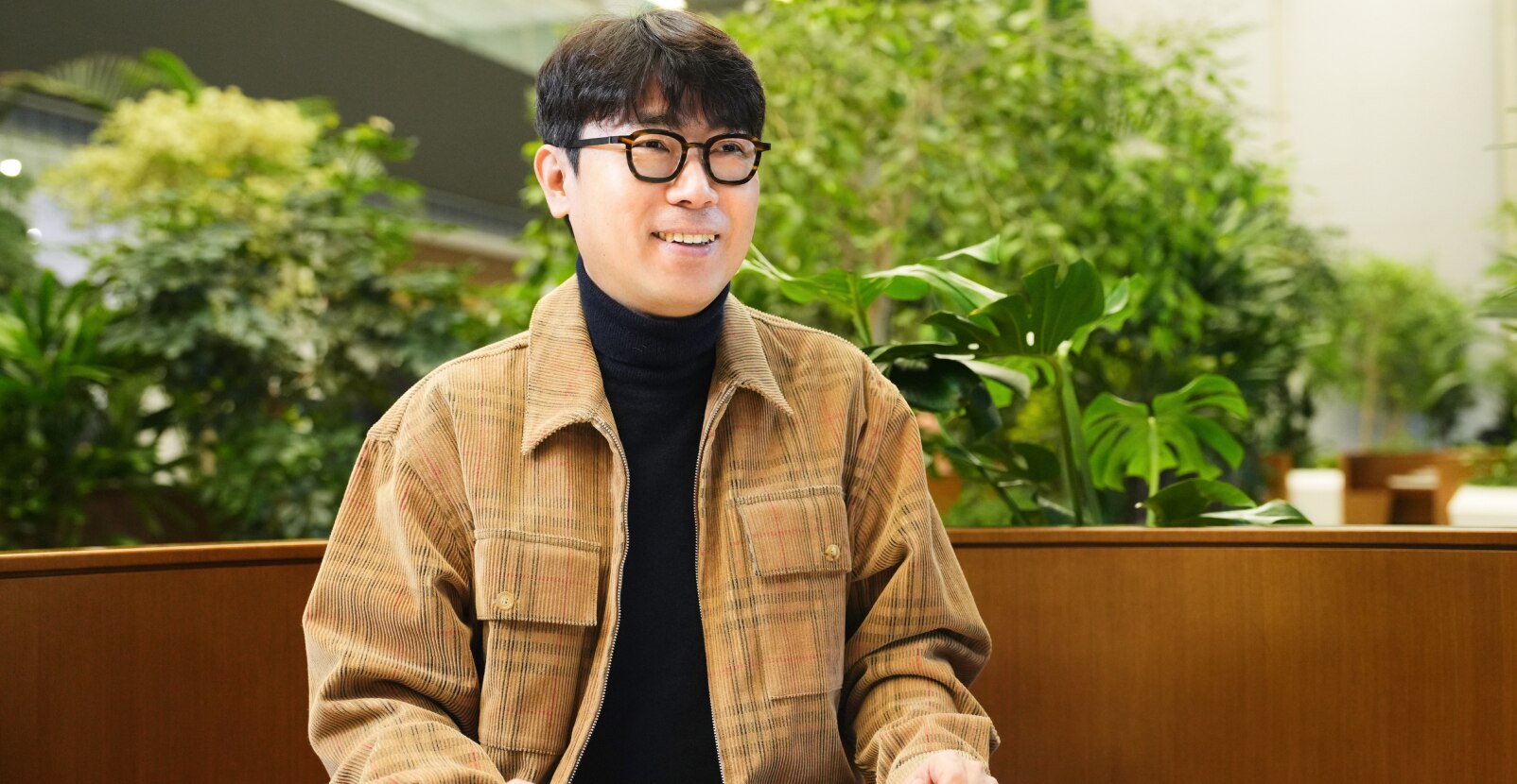 传感器设计团队的任务负责人坐在满是植物的室内工作空间里，在面试中微笑。