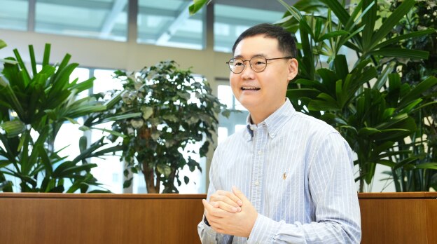 安全与电力产品开发团队的任务负责人Stanley Yoo，戴着眼镜，穿着条纹衬衫，在被绿色植物包围的办公空间里发言