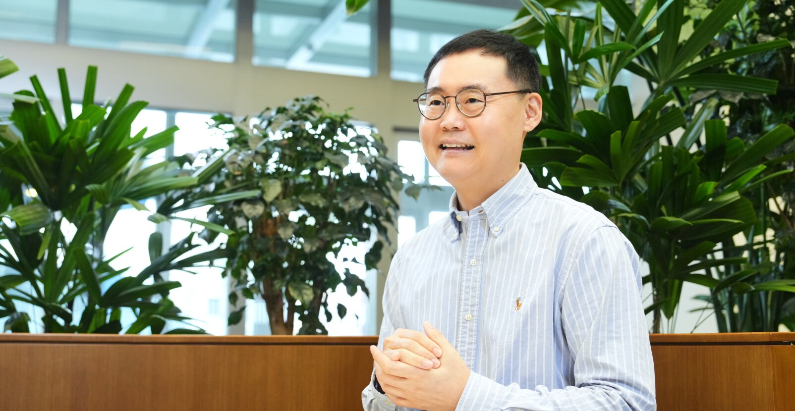 安全与电力产品开发团队的任务负责人Stanley Yoo，戴着眼镜，穿着条纹衬衫，在被绿色植物包围的办公空间里发言