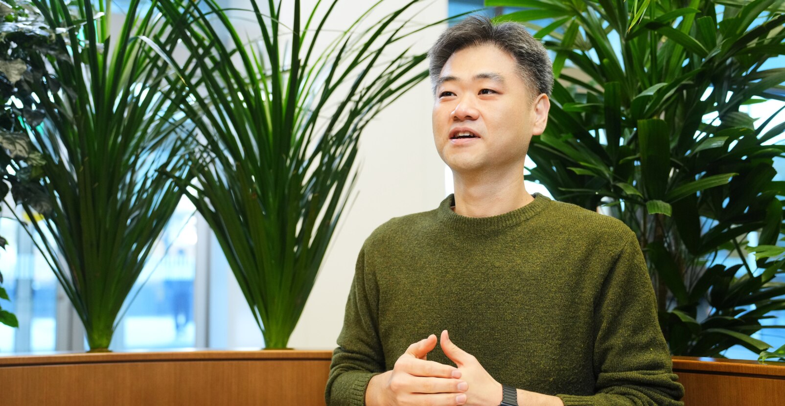 安全与电力产品开发团队的任务负责人姜贤宰，身穿绿色毛衣，在布满植物的办公室里以轻松的表情说话