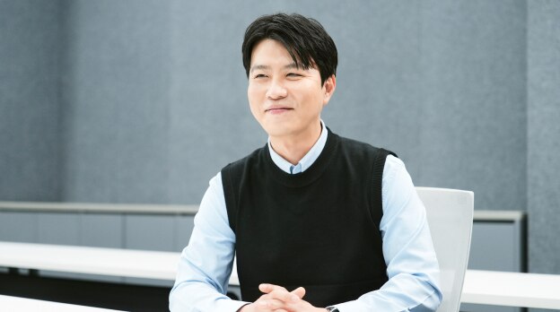 A project leader from the Memory Product Planning Team is smiling while seated in a modern office with a soft gray background.