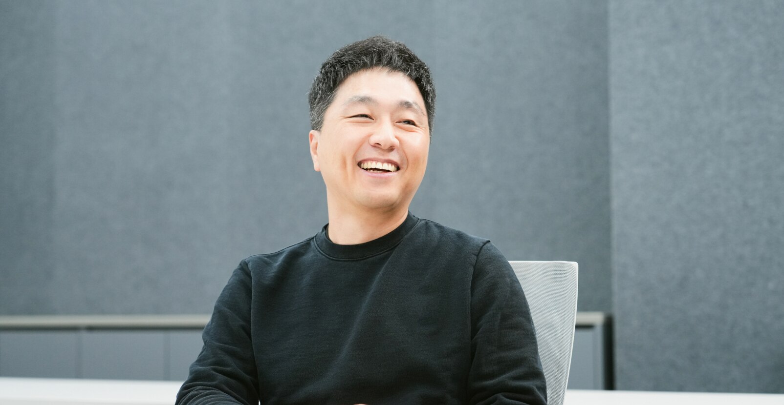 A project leader from the Advanced DRAM Technology Team is seated in a conference room, smiling brightly.