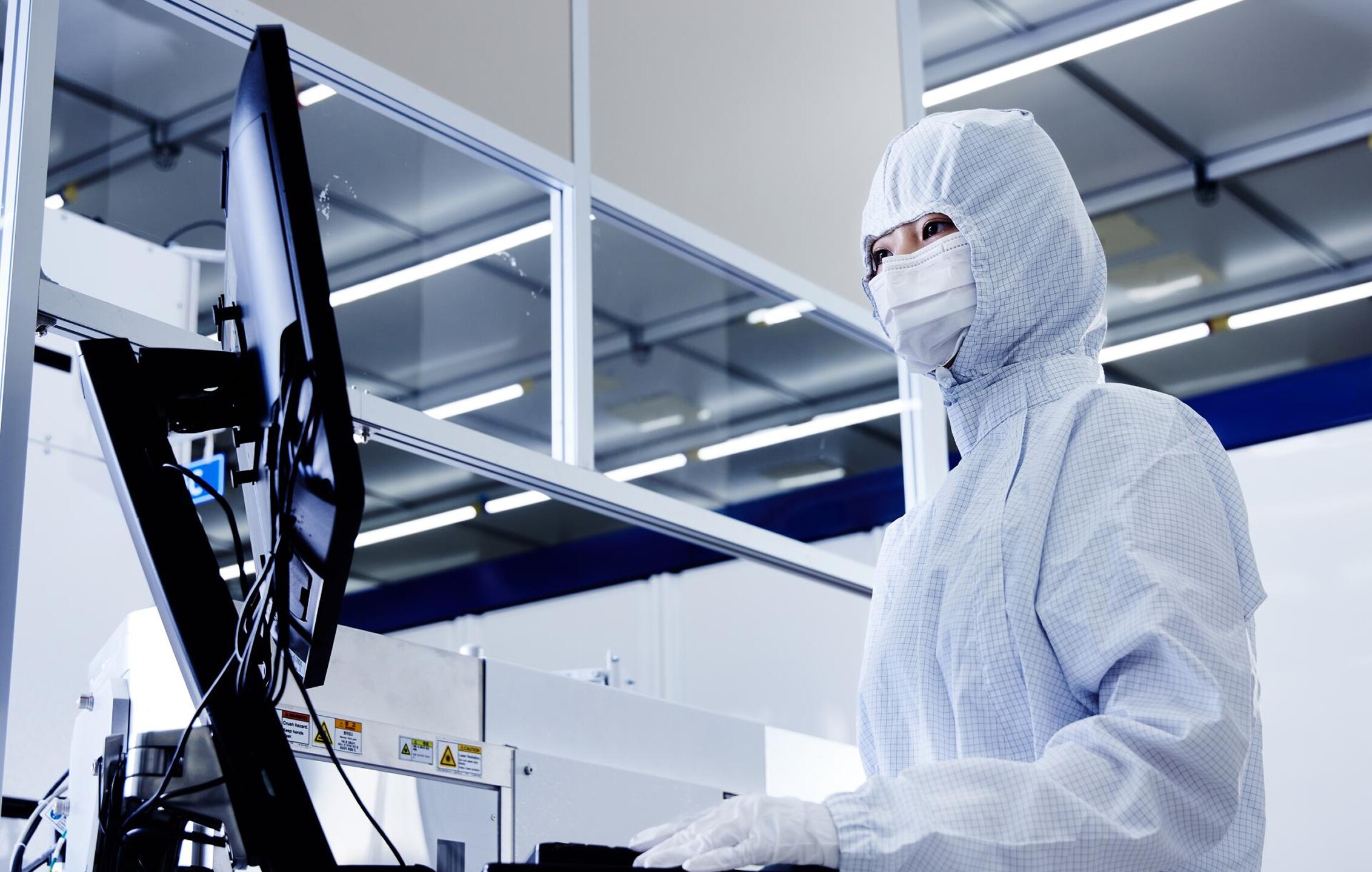 身着全套无尘服和口罩的工人在半导体晶圆厂无尘车间内通过电脑屏幕监控生产工艺数据.