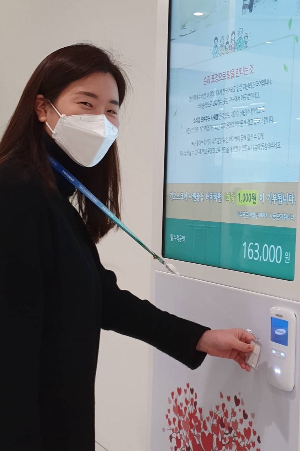 A Samsung Semiconductor employee is holding her employee ID card to the donation kiosk to make a donation