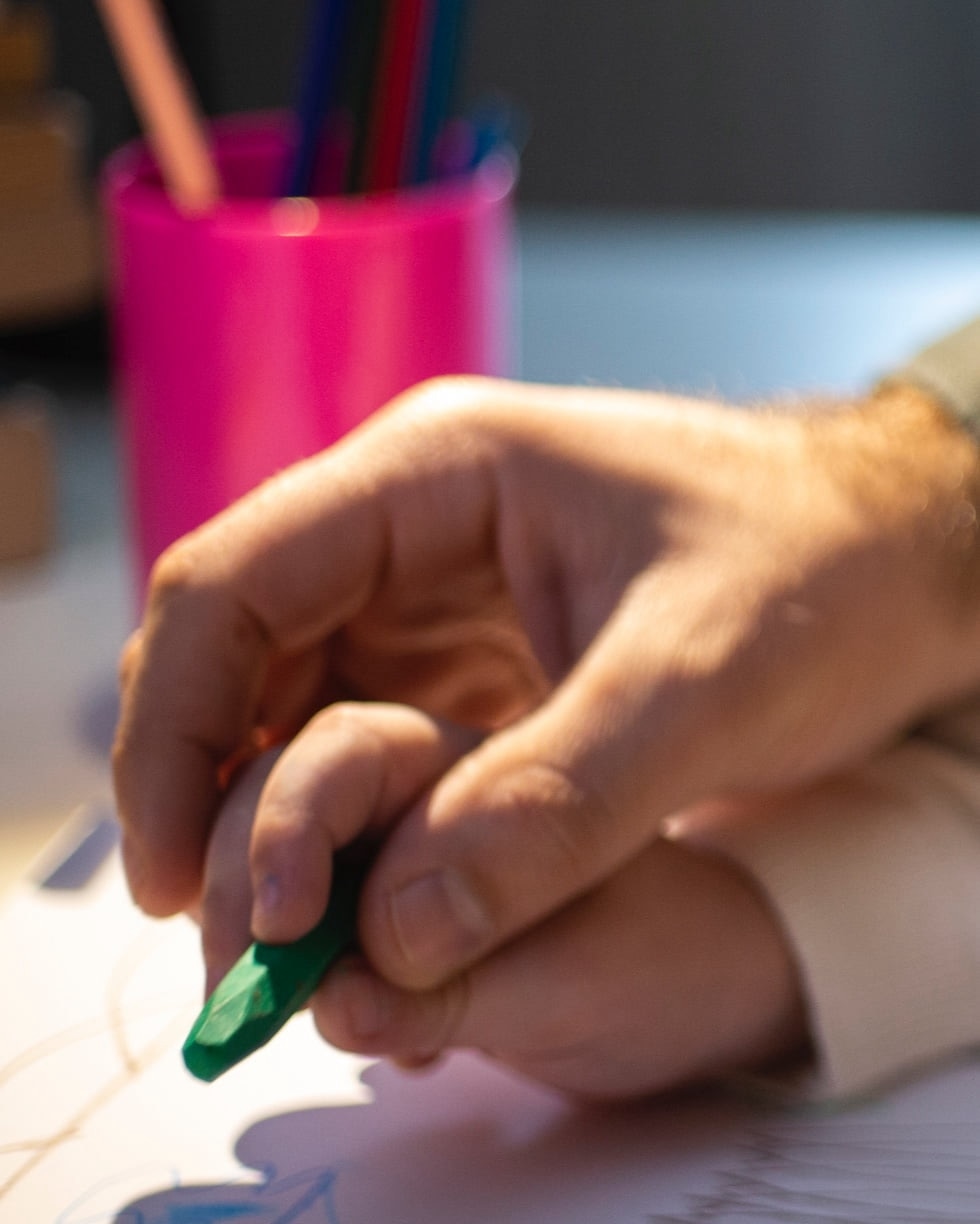 An adult's hand is helping a child's hand draw with a crayon