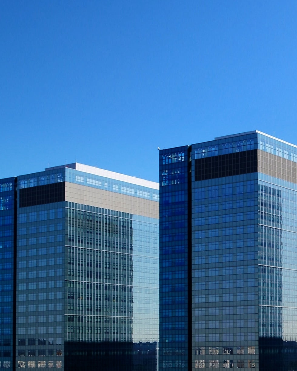 Two tall office buildings seen against a blue sky.