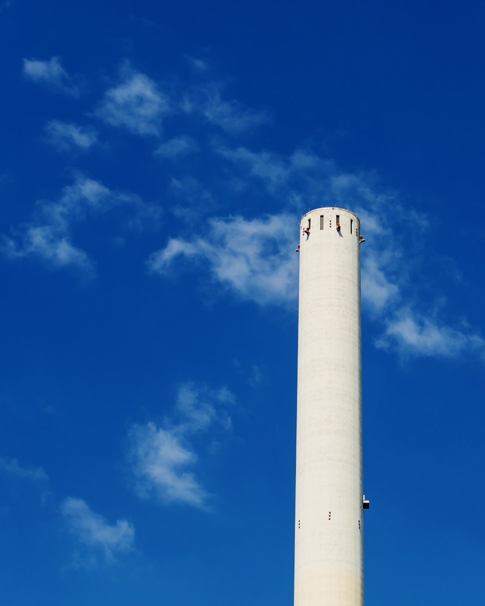 一座高耸的白色圆柱形塔楼耸立在湛蓝的天空下，天空中点缀着零星的云朵。